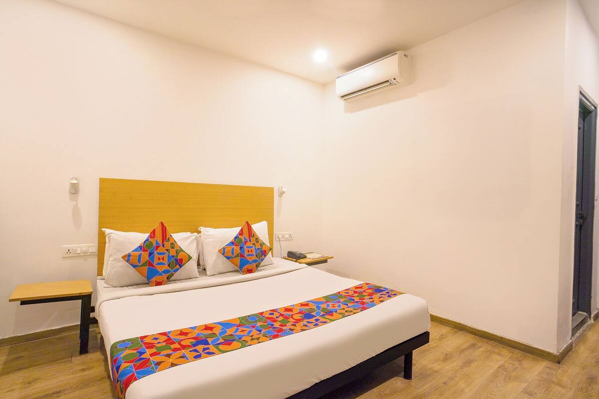 A neatly made bed with a colorful geometric-patterned bedspread, a wooden headboard, and a bedside table with a lamp.