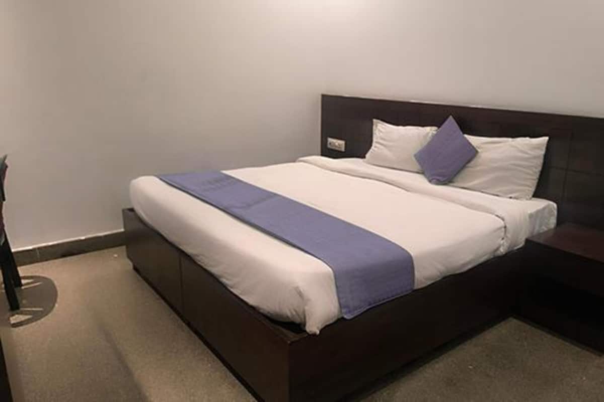 Cama bem arrumada com manta azul, almofadas brancas e cabeceira escura.