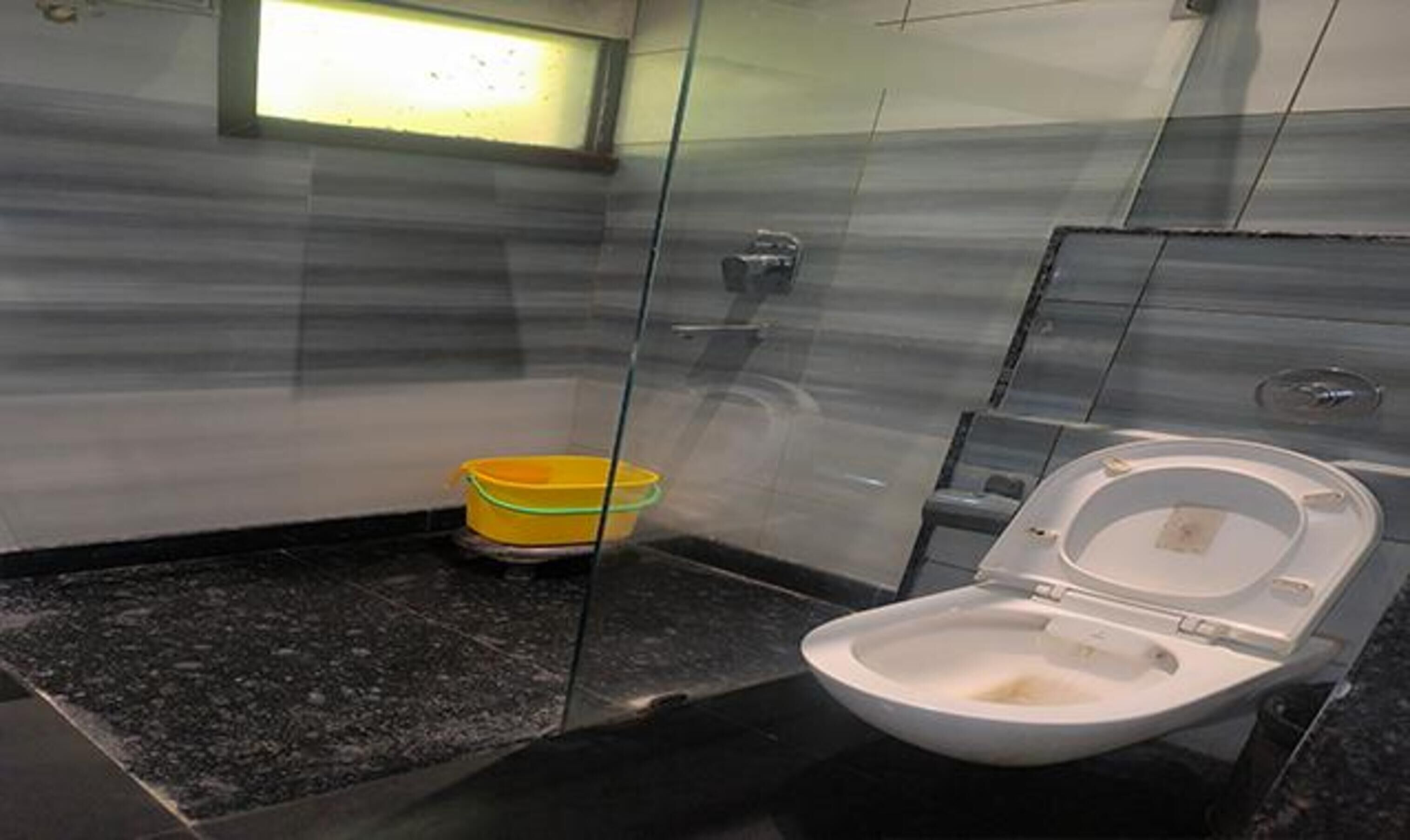 A small bathroom with a toilet, a yellow bucket, and a glass partition.