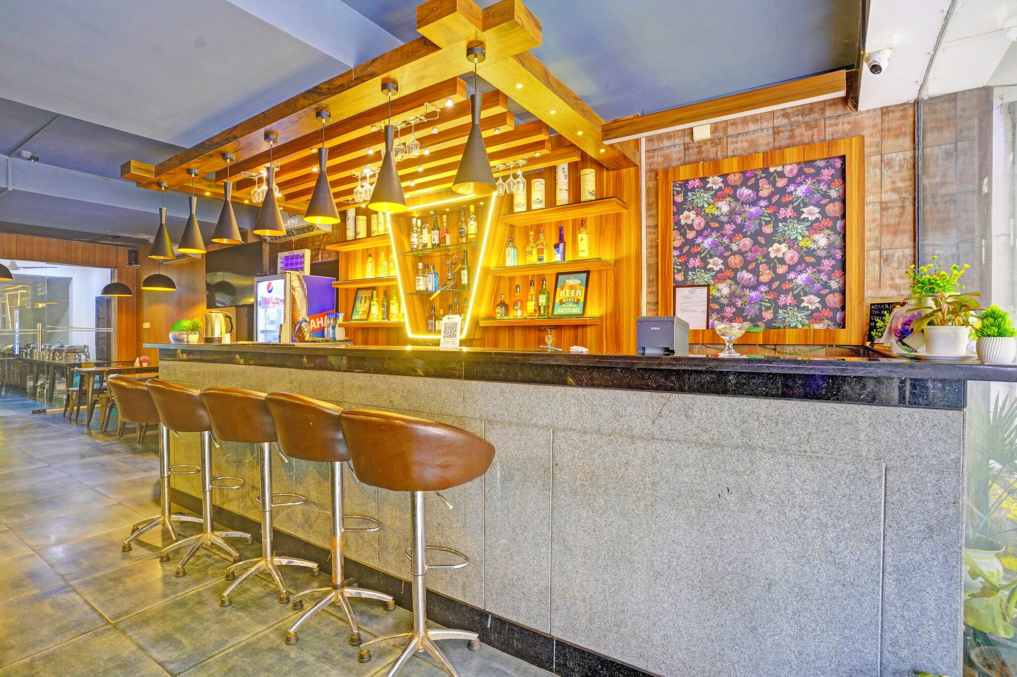 A bar area with a counter, stools, and a floral wall decoration.