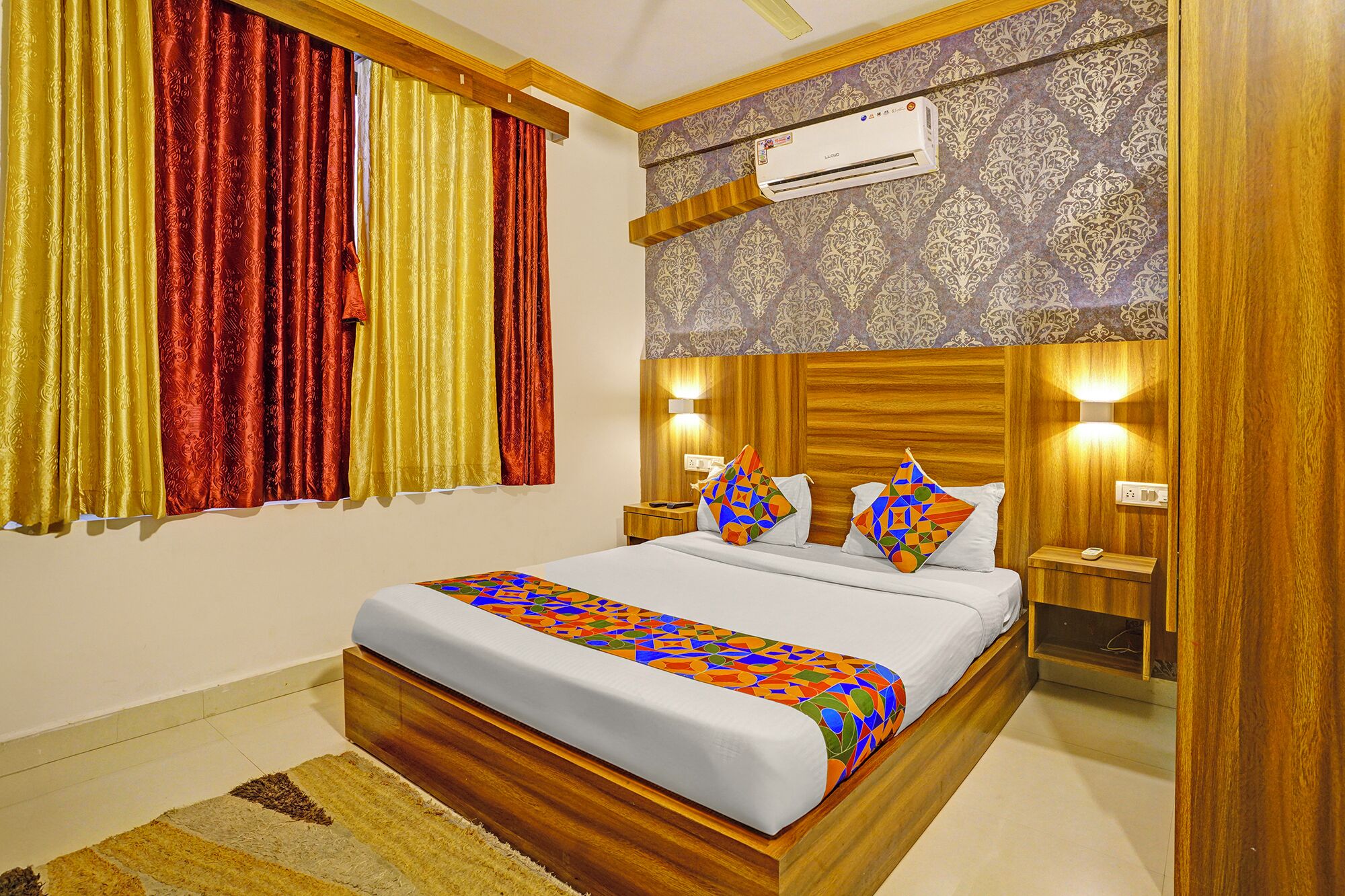 A hotel room with a wooden bed frame, a patterned wall, and a window with red and yellow curtains.