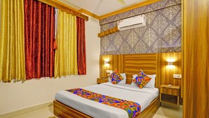 A hotel room with a wooden bed frame, a patterned wall, and a window with red and yellow curtains. - Fabhotel Tranquil Inn (Calangute)