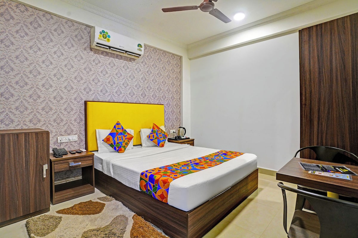 A hotel room with a bed, a desk, a chair, a nightstand, an air conditioning unit, and a ceiling fan.