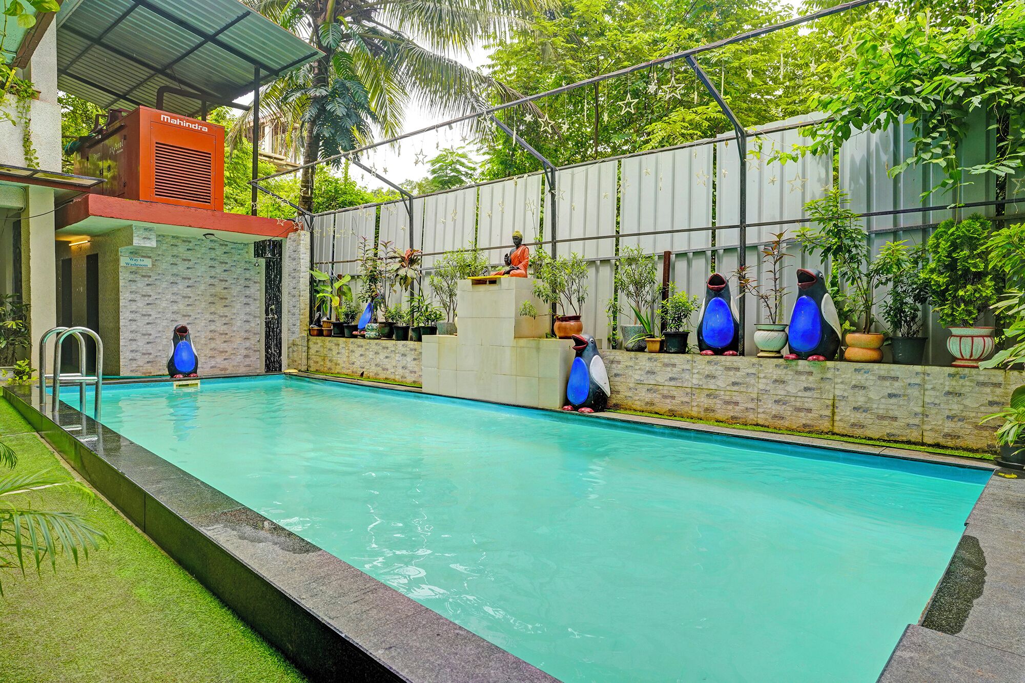 A swimming pool with a metal roof, surrounded by potted plants and a statue.