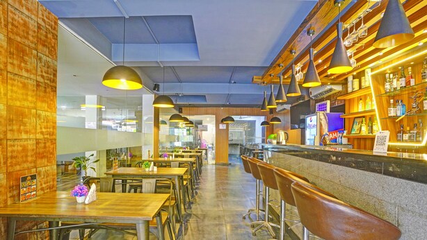 A restaurant interior with high tables, bar stools, pendant lighting, and a bar area with shelves of bottles. - Fabhotel Tranquil Inn (Calangute)
