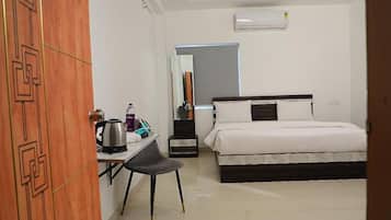 A hotel room with a bed, a desk with a chair, a mirror, and an air conditioning unit.
