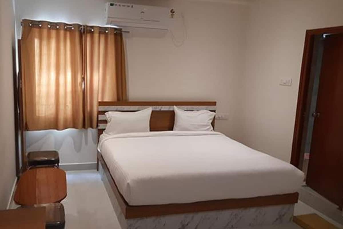 Een slaapkamer met een bed, een houten nachtkastje, een stoel, een raam met gordijnen en een airconditioner.