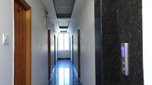 En smal hall med en trädörr på vänster sida, ett svart kylskåp på höger sida och ett fönster längst in.