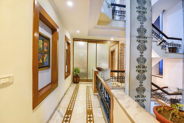 A hallway with a tiled floor, wooden doors, and a staircase with a metal railing. - Fabhotel Siris 18 (Gurugram)