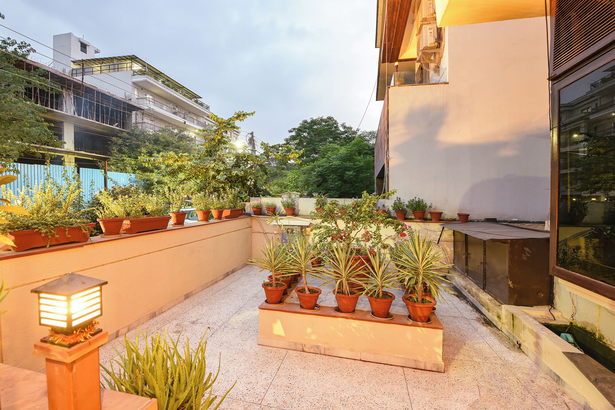 A rooftop garden with potted plants and a small table, surrounded by a building with balconies.