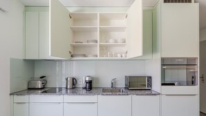 Una cocina moderna con armarios blancos, horno empotrado, cafetera, tostadora y microondas.