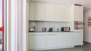 Una cocina compacta con armarios blancos, microondas, cafetera y tostadora.