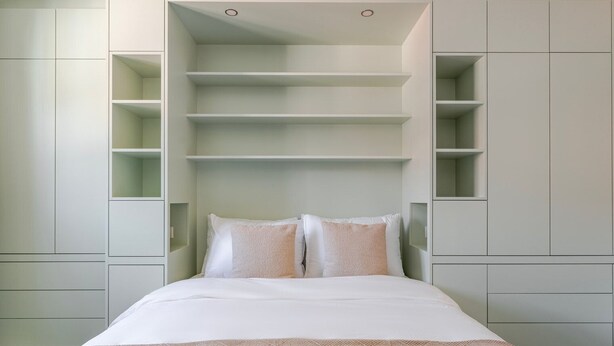 Un dormitorio con cama, ropa de cama blanca y estanterías empotradas.