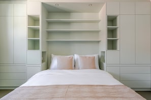 A bedroom with a bed, white bedding, and built-in shelving.