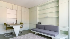 Una habitación moderna y compacta con un sofá gris, una mesita y una silla. Hay estantes empotrados en las paredes.