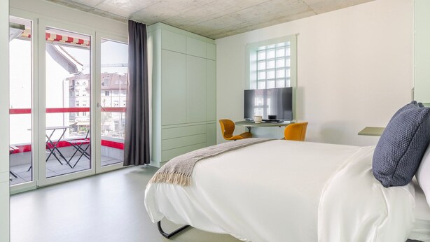 A bedroom with a bed, a TV, and a balcony with a table and chairs.