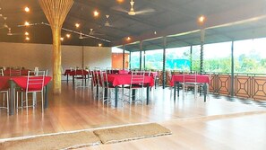 A spacious indoor area with rows of tables and chairs, large windows, and a ceiling fan.