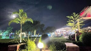 A nighttime outdoor area with illuminated plants and a building in the background. - Shayan Resort (Singair)