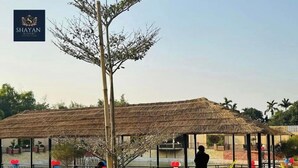 A restaurant with a thatched roof, outdoor seating, and a view of the surrounding greenery. - Shayan Resort (Singair)
