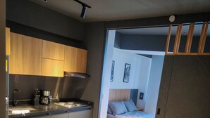 A modern kitchen with wooden cabinets, a coffee machine, and a stove. There is a bed with a headboard and pillows in the adjacent room. - Exclusive apartment Cartagena de Indias. (Cartagena de Indias)