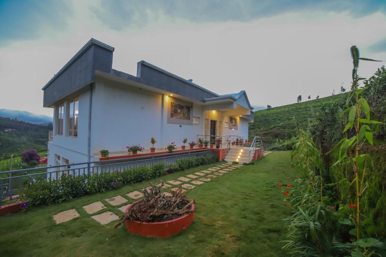 Uma casa moderna de dois andares com um jardim bem cuidado, uma escadaria que leva à entrada e vista para a paisagem ao redor.