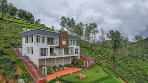 Un moderno edificio de dos pisos con techo plano, rodeado de exuberantes plantaciones de té y árboles.