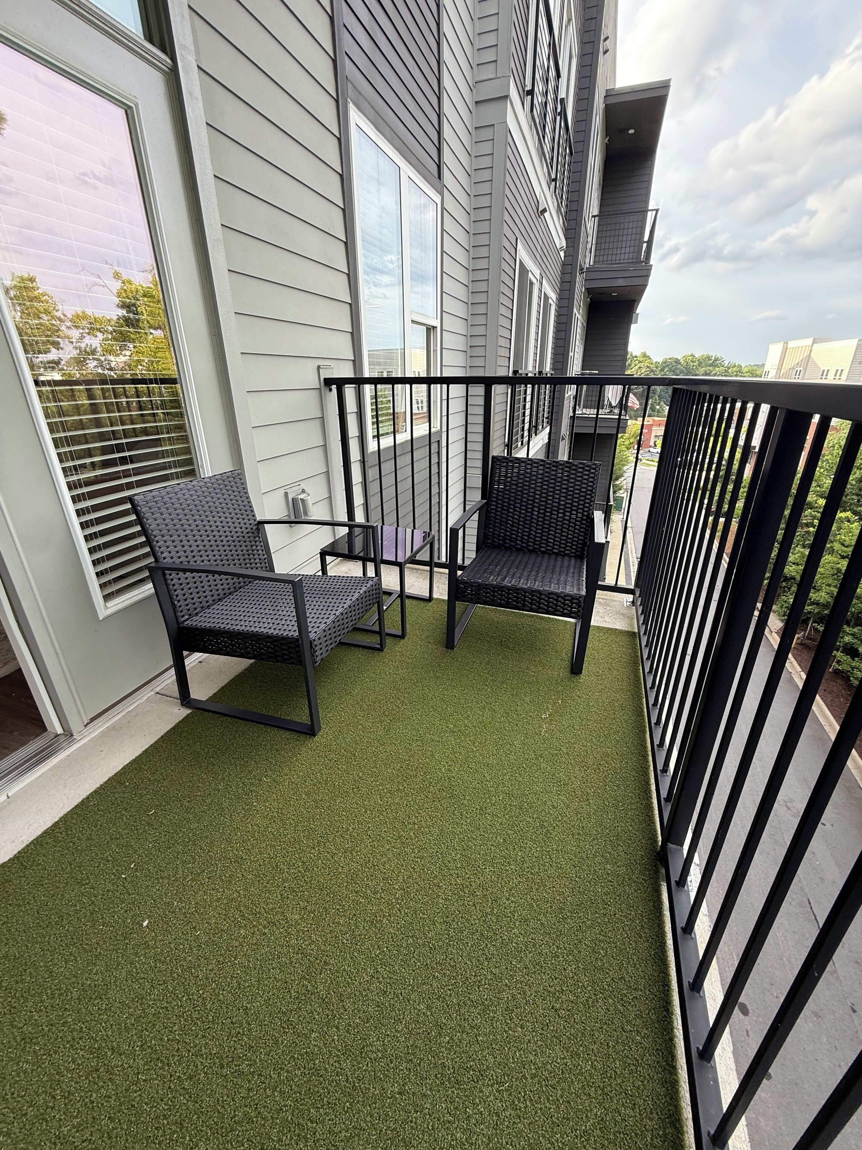 A balcony with artificial grass, two black chairs, and a railing.