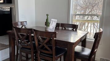 A dining area with a wooden table and chairs, a chandelier, and a view of trees through a window.