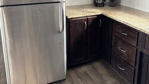A kitchen with dark wooden cabinets, a stainless steel refrigerator, a granite countertop, and a coffee maker. -  Lakefront Cottage on Lake Winnebago (Hilbert)