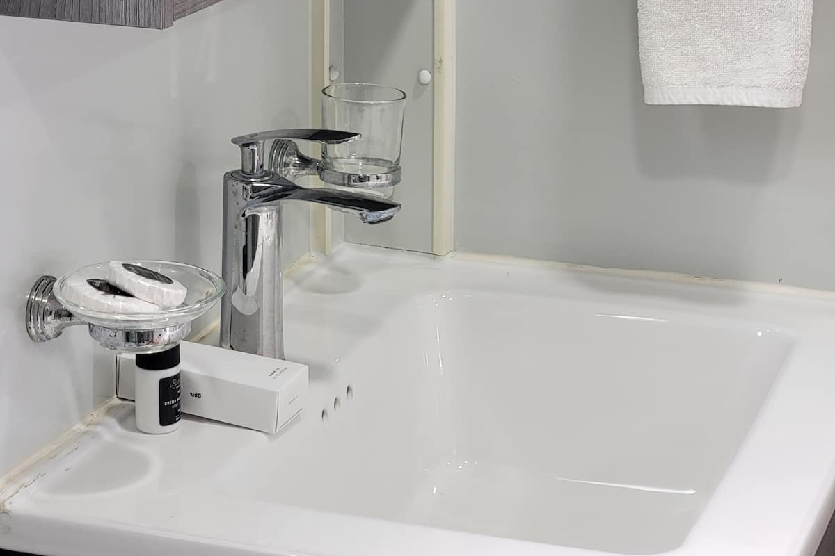 A modern bathroom with a white sink, chrome faucet, and a glass soap dispenser.