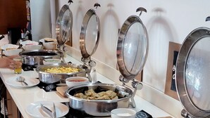 A buffet setup with various dishes in metal containers, utensils on plates, and a lime bowl. - ZURBAN TRAVELERS (Paraíso)