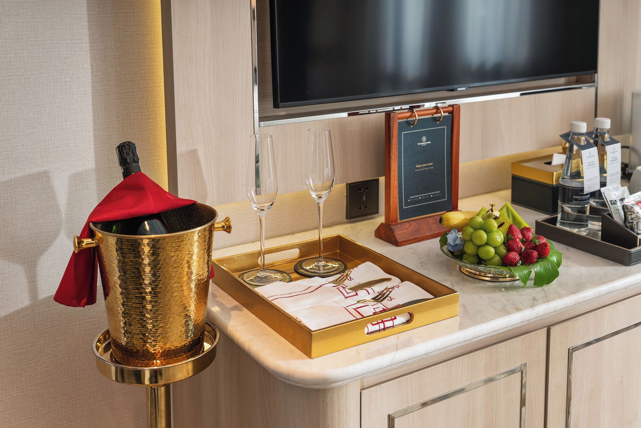 A hotel room with a minibar, a television, and a fruit bowl on the counter.