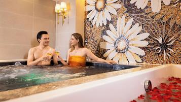 A couple in a hot tub with a mosaic wall behind them.
