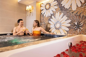 A couple in a hot tub with a mosaic wall behind them.