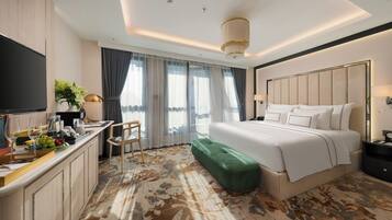 A hotel room with a bed, a desk with a chair, a television, and a large window with curtains.