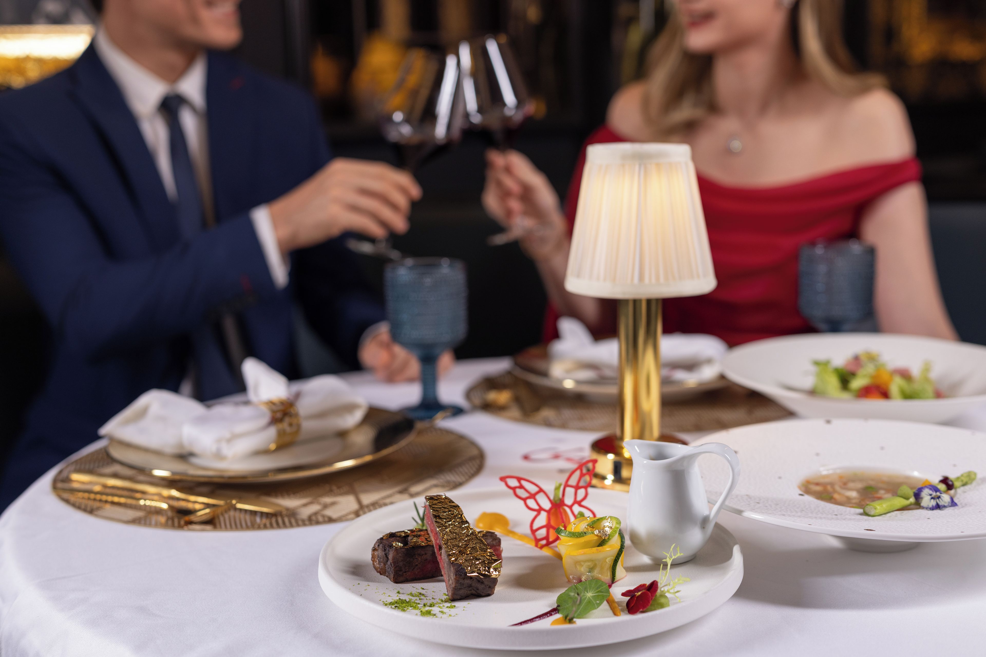 A dining table with plates of food, a lamp, and wine glasses.