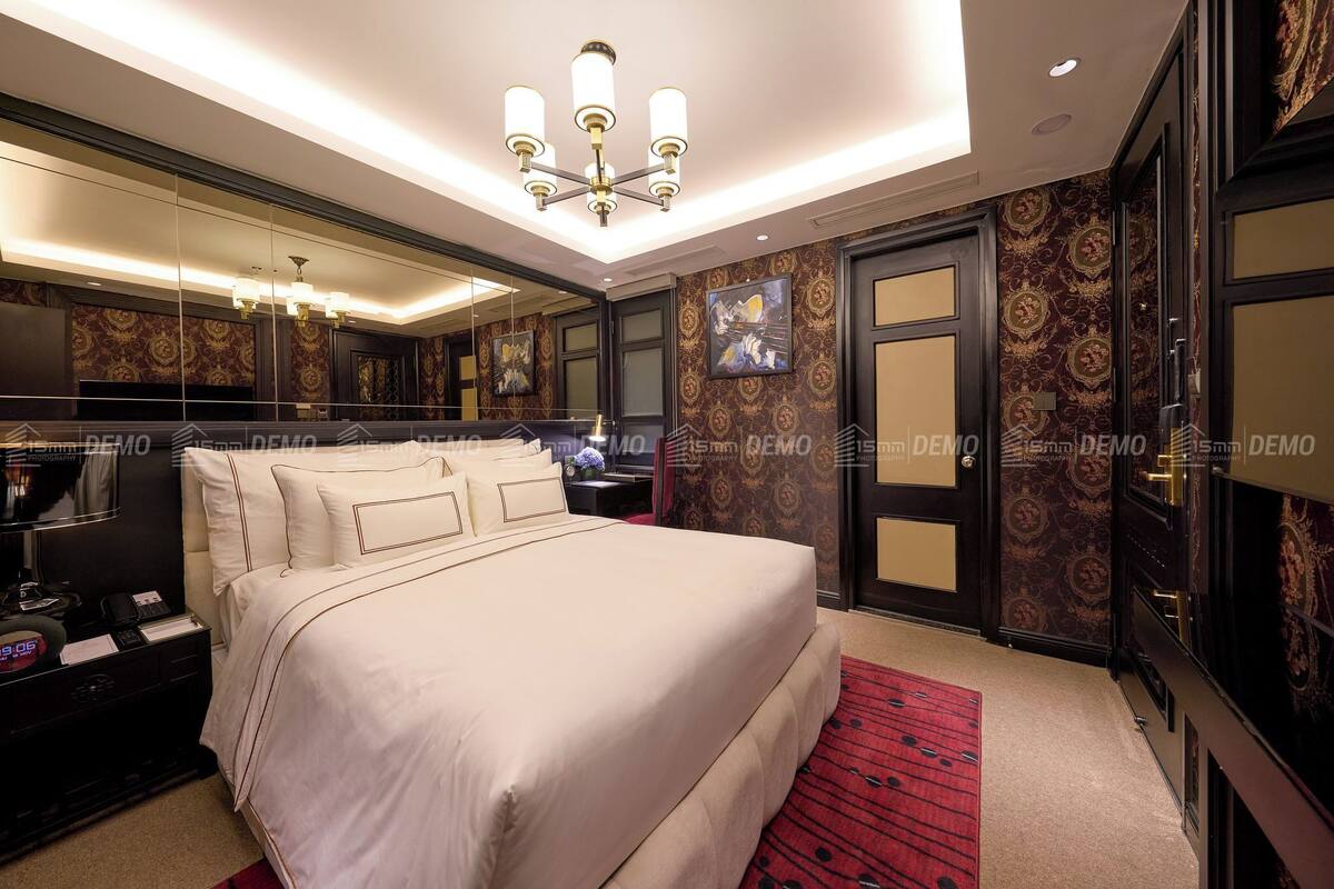 A hotel room with a large bed, a bedside table with a lamp, a mirror, and a red carpet.