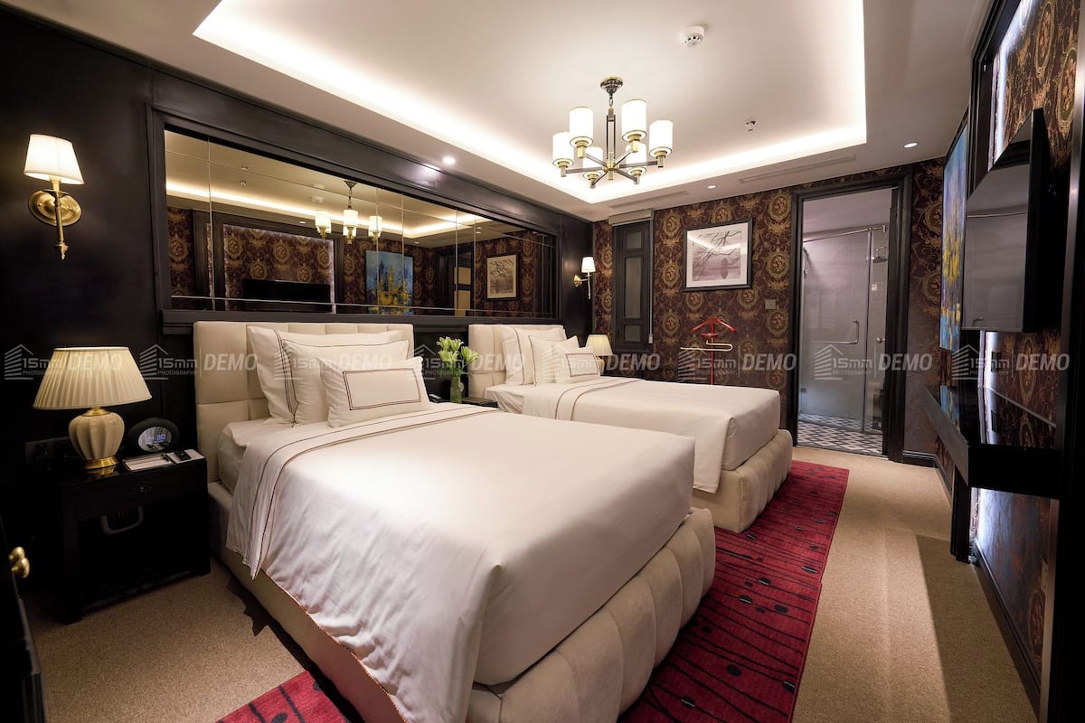 A modern hotel room with two beds, a large mirror, a chandelier, and a red carpet.