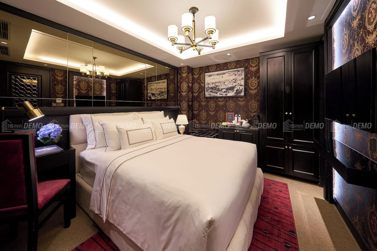 A spacious bedroom with a large bed, a vanity with a mirror, and dark wood cabinets.