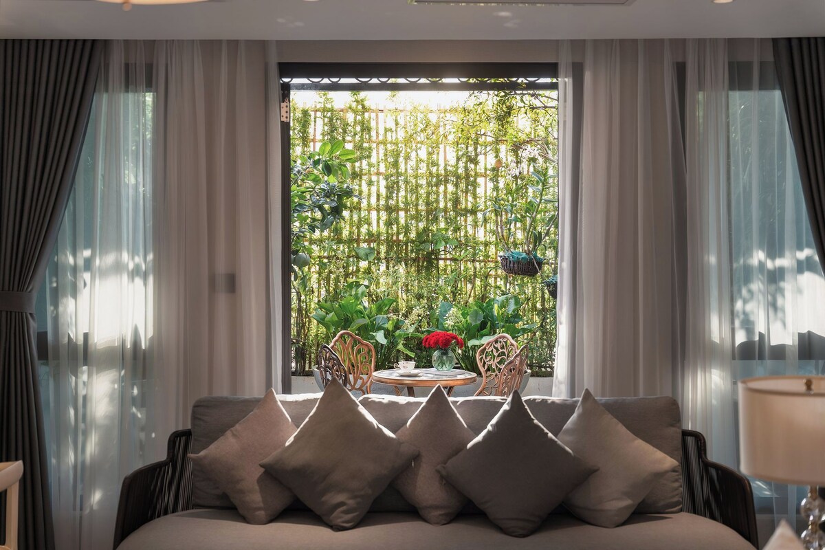 Una habitación con cama, una mesa con sillas y vistas a un jardín por la ventana.