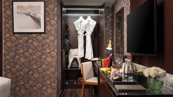 A hotel room with a bed, a desk with a chair, a television, and a hair dryer on the wall.