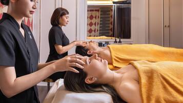 A massage therapy session in a room with a bed, a massage table, and a mirror.