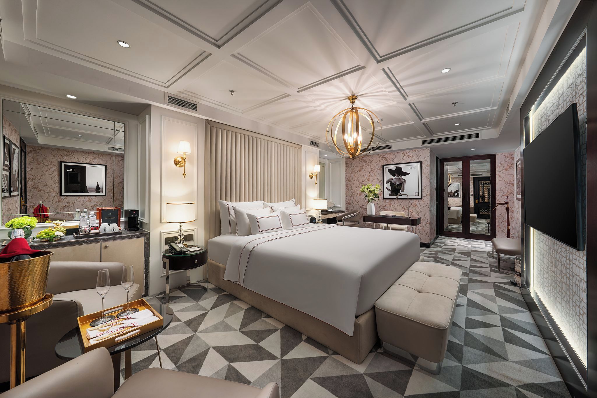 Une chambre d’hôtel moderne dotée d’un grand lit, d’un coin salon, d’un bureau avec une chaise, d’une télévision et d’une salle de bain visible à travers une porte ouverte.