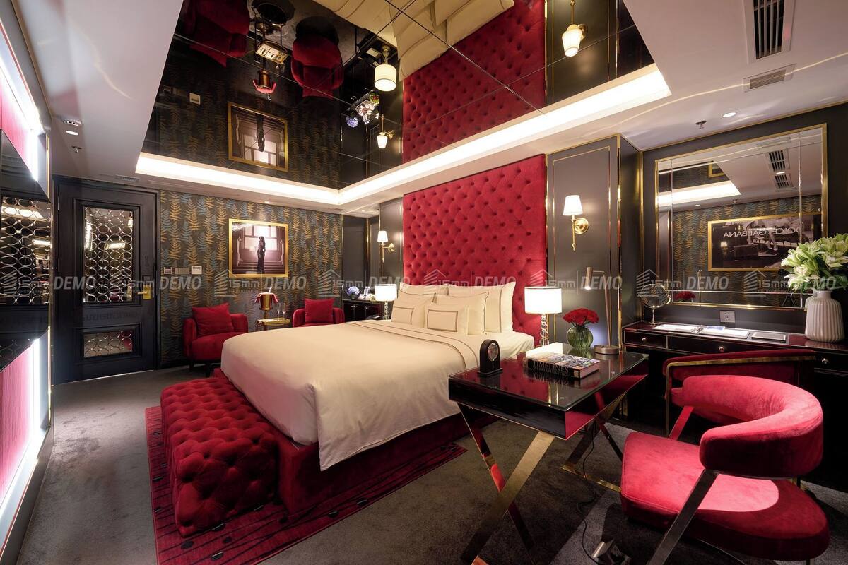 A luxurious bedroom with a large bed, red upholstered chairs, a vanity, and a mirror.