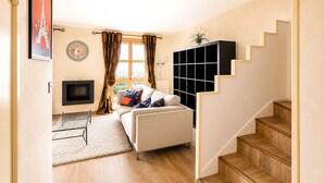 A living room with a sofa, a TV, a window with curtains, a staircase, and a wall-mounted shelf.