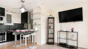 A modern kitchen with a dining area, a TV mounted on the wall, and a glass shelf unit.