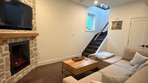 Una sala de estar con chimenea de piedra, un televisor de pantalla plana, un sofá y una escalera que conduce a un nivel superior.