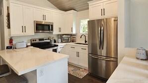 Una cocina moderna con armarios blancos, electrodomésticos de acero inoxidable y techo de madera.