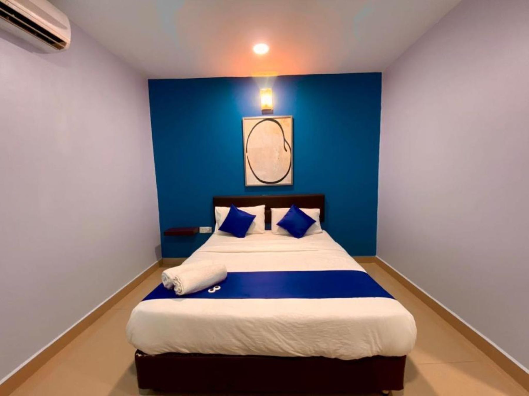 Un lit bien fait, avec une literie blanche et bleue, un mur d’accent bleu et une seule œuvre d’art au-dessus du lit.