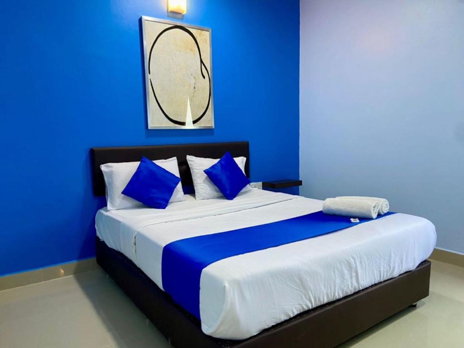 Une chambre d’hôtel avec un grand lit, des murs bleus et une œuvre d’art encadrée au-dessus du lit.